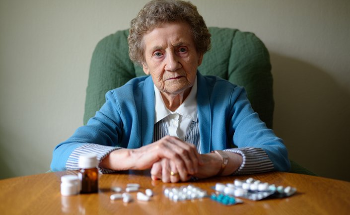 Пожилая женщина сидит напротив таблеток